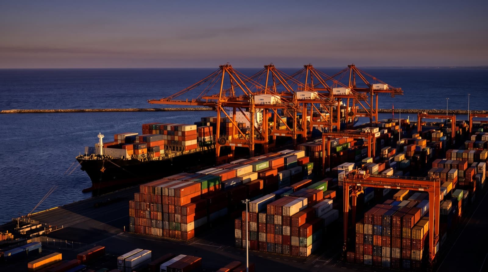 Container terminal at Fremantle Port near Perth at sunset with orange gantry cranes and a container ship at berth